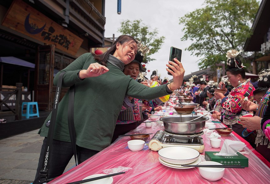 10月31日，游客在丹寨縣萬達小鎮長桌宴上與苗族同胞合影。