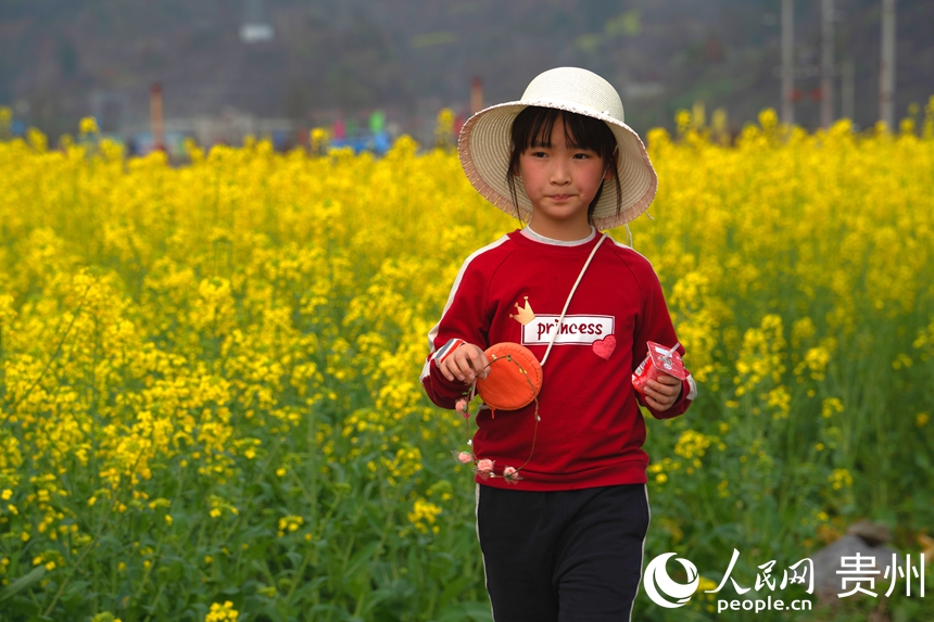 游客站在田坎上與盛放的油菜花合影。人民網 陽茜攝