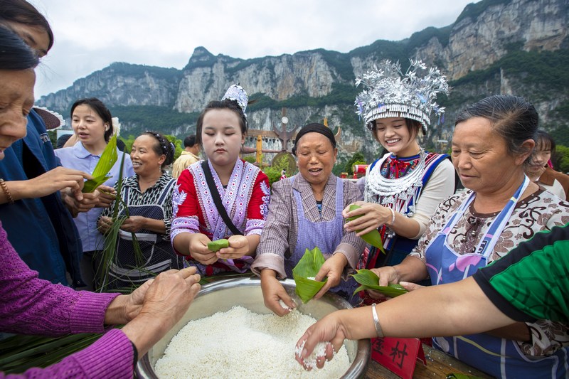 6月7日，貴州省畢節市黔西市新仁苗族鄉化屋村，村民們和游客包粽子。